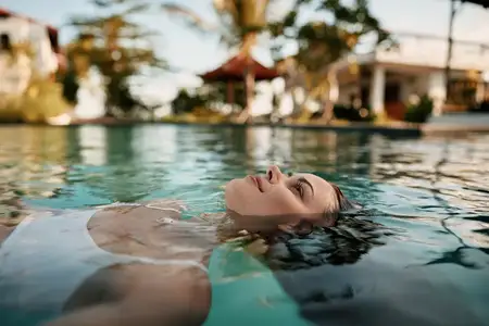 Крупный план воды, окружающей безмятежную пловчиху, передающий отдых, оздоровление и безмятежность в обстановке курортного бассейна