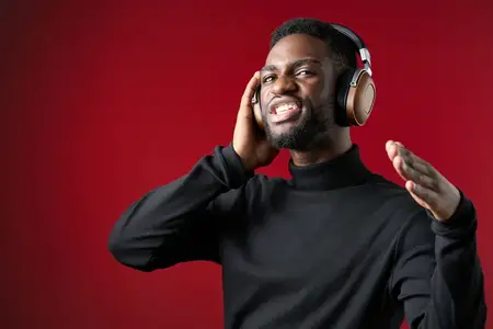 Радостный мужчина в наушниках, погруженный в музыку, на фоне ярко-красного фона, выражающий энергию и счастье, представляющий концепции музыки и образа жизни