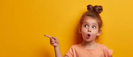 Удивлённая маленькая девочка указывает пальцем на что-то на ярко-жёлтом фоне, есть место для текста