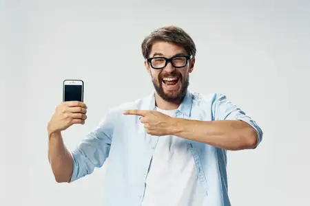 Веселый эмоциональный мужчина держит в руках телефон, олицетворяя технологии, общение, гаджеты и звонки