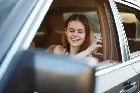 Веселая молодая женщина отдыхает в автомобиле с закрытыми глазами и улыбкой, одетая в повседневную одежду, воплощая радость и беззаботный дух в яркой солнечной обстановке