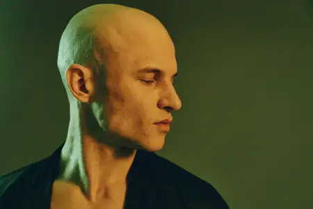 Этот захватывающий портрет запечатлевает лысого мужчину с безмятежным выражением лица на фоне мягко освещенного заднего плана