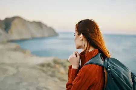 Женщина путешествует с рюкзаком рядом с морем в горах на природе