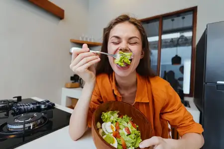 Радостная модель наслаждается свежим салатом на современной кухне, что подчёркивает здоровое питание, яркие цвета и выбор в пользу здорового образа жизни