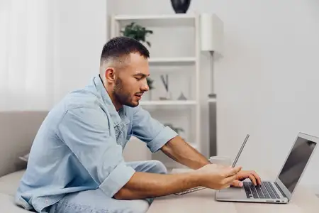 Сосредоточенный мужчина погружен в работу на ноутбуке дома в окружении современного минималистичного декора