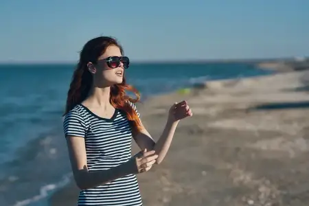 Портрет женщины в футболке и очках на пляже в горах у моря