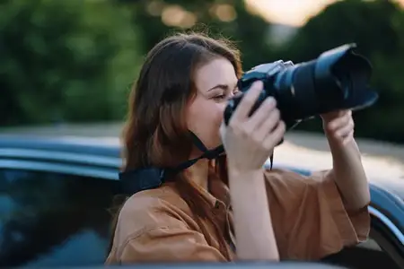 Юная женщина-фотограф улыбается, делая снимки зеркальной камерой DSLR в красивом уличном освещении