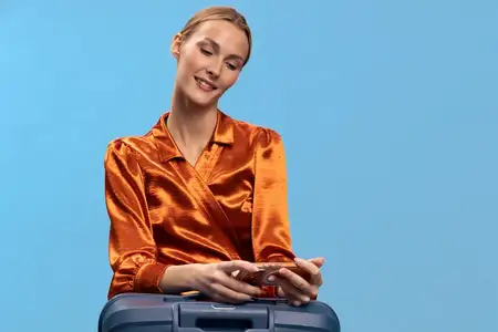 Счастливая молодая женщина в оранжевой атласной блузке положила руки на чемодан