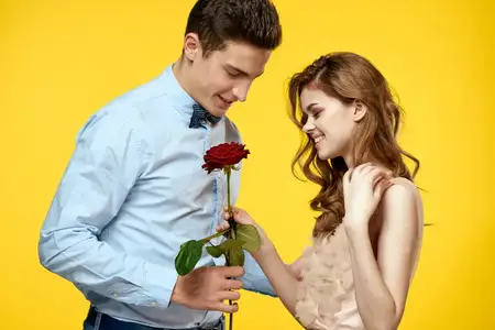 Любящая молодая пара с красной розой в руках обнимается на жёлтом фоне