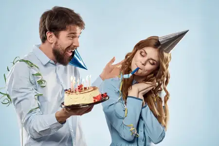 Мужчина и женщина в праздничных колпаках на синем фоне с тортом и свечами