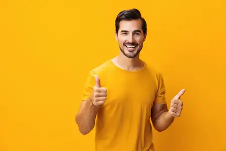 Улыбающийся мужчина, счастливый, в жёлтой футболке, поднимает руку на фоне