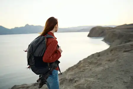 Путешествия, туризм: молодая женщина с рюкзаком у моря в горах на природе
