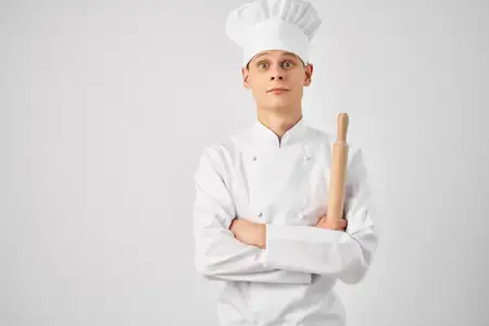 Шеф-повар в белом колпаке на голове, кухонная утварь, процесс приготовления