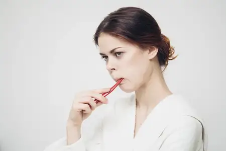 Женщина с зубной щеткой во рту на светлом фоне, одетая в белый халат
