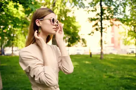 Красивая женщина в солнечных очках и шляпе на зелёной траве в парке