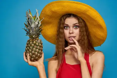 Женщина в желтой шляпе с ананасом в руках, эмоции, веселье, образ жизни, лето, фрукты, голубой фон