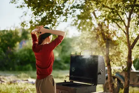 Молодой человек стоит у гриля для барбекю на яркой outdoor-сцене, демонстрируя повседневный летний наряд