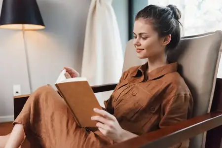 Молодая женщина в стильном коричневом наряде отдыхает, читая книгу в современном уютном пространстве