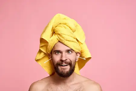 Мужчина с желтым полотенцем на голове, губка, уход за кожей, розовый фон