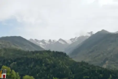 Горный лесной пейзаж с облаками, вершинами, небом и долиной, открывающий живописную панораму с далекими заснеженными пиками