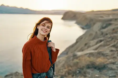 Счастливая женщина-туристка в красном свитере отдыхает в горах на природе рядом с морем
