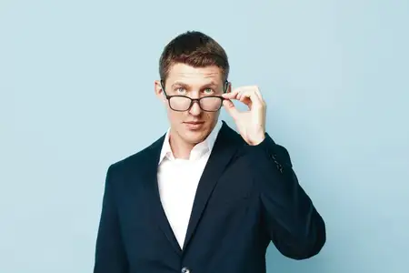 Мужчина улыбается на фоне, одет в повседневную одежду, выглядит современно, модно и уверенно