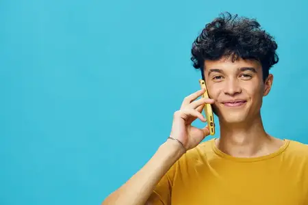 Веселый молодой человек пользуется желтым смартфоном и улыбается