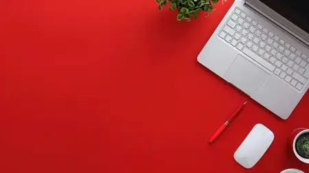 Современное рабочее пространство с красным столом, ноутбуком, чашкой кофе и различными офисными принадлежностями, вид сверху