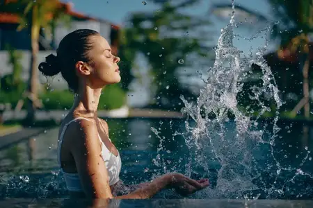 Женщина в купальнике играет с брызгами воды в залитом солнцем бассейне