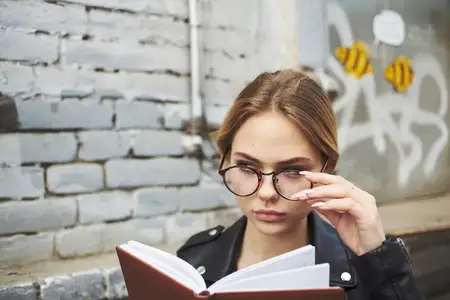 Женщина в черной куртке с блокнотом в руках возле кирпичного здания, обрезанный вид