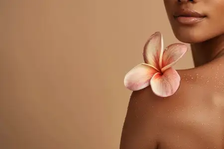 Безмятежный крупный план, подчеркивающий плечо женщины с нежным цветком на теплом бежевом фоне