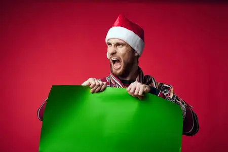 Эмоциональный мужчина в шапке Санты на зелёном фоне