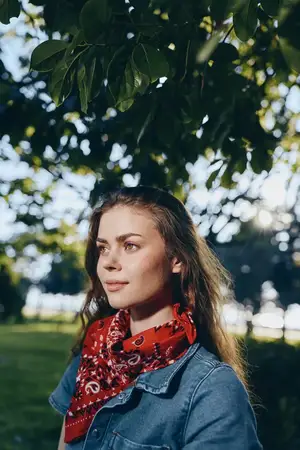 Молодая женщина, ведущая активный образ жизни, одетая в современный бохо-вестерн деним и красную бандану, задумчиво стоит под густой листвой