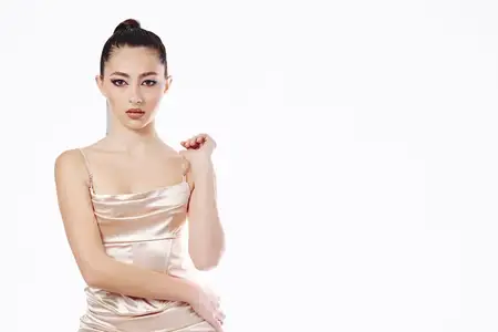 Стильная модель в шелковом бежевом платье демонстрирует креативную концепцию красоты в минималистичной студийной обстановке