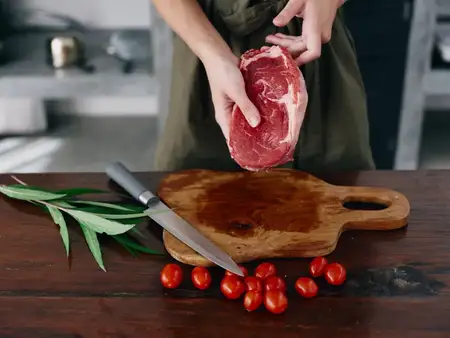 Женщина с ножом в руке нарезает свежий стейк из мяса для жарки на кухне