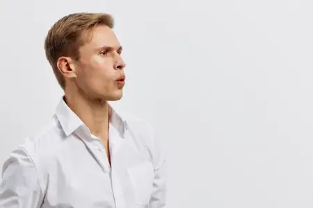 Задумчивый молодой светлокожий мужчина в белой рубашке смотрит в сторону с сосредоточенным выражением лица, изолированный на однотонном белом фоне