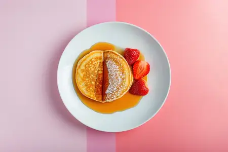 Вкусные панкейки, украшенные сиропом и клубникой, красиво выложенные на минималистичной белой тарелке, созданы для эстетики красочного завтрака, привлекающей любителей еды