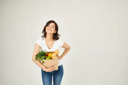 Симпатичная женщина в белой футболке с пакетом продуктов пользуется услугой доставки покупок