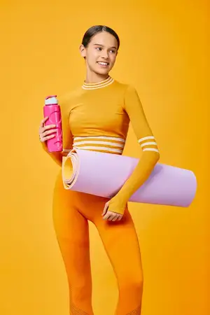 Спортивная спортсменка с ковриком и бутылкой позирует для фитнес-режима, энергии и растяжки в смелой студийной сцене с яркими цветами и динамичным движением