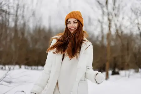 Жизнерадостная женщина в зимней одежде и шапке наслаждается прогулкой по зимнему лесу