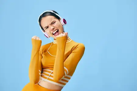 Спортивная девушка-атлет в стильной тренировочной одежде принимает энергичную позу, демонстрируя силу и уверенность, слушая музыку, портрет здорового активного образа жизни в минималистичном синем…
