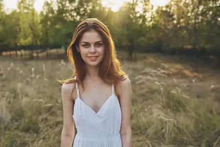 Счастливая путешественница отдыхает в поле на природе, на заднем плане деревья, она жестикулирует руками