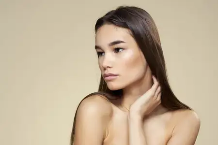 Симпатичная женщина с обнаженными плечами, косметикой, чистой кожей и уходом за волосами на бежевом фоне