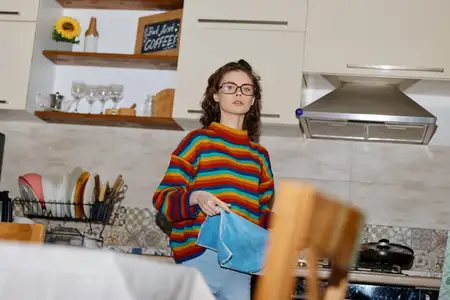 Сцена запечатлевает женщину дома на современной кухне, естественный момент повседневной жизни, который подчеркивает уют и повседневный стиль, пока она раскладывает одежду на чистой столешнице