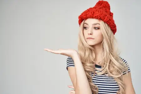 Красивая женщина в модной одежде и красной шляпе на светлом фоне