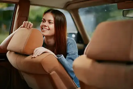 Счастливая молодая женщина в джинсовой куртке наслаждается временем в машине, в которую проникает естественный свет, создавая радостную и безмятежную атмосферу во время непринужденной поездки