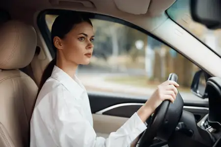 Улыбающаяся женщина-водитель держит руки на рулевом колесе внутри автомобиля в дневное время