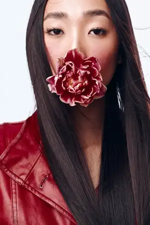 Женщина с длинными чёрными волосами и в красной кожаной куртке держит цветок во рту