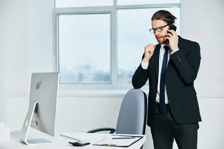 Мужчина-менеджер в деловом костюме работает в офисе, используя телефон и технологии