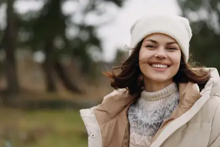 Веселая женщина на открытом воздухе в теплом пальто и шерстяной шапке, откровенный портрет на фоне нежного пейзажа, расслабленный стиль, ветер в волосах, спокойный парковый фон, безмятежное и…